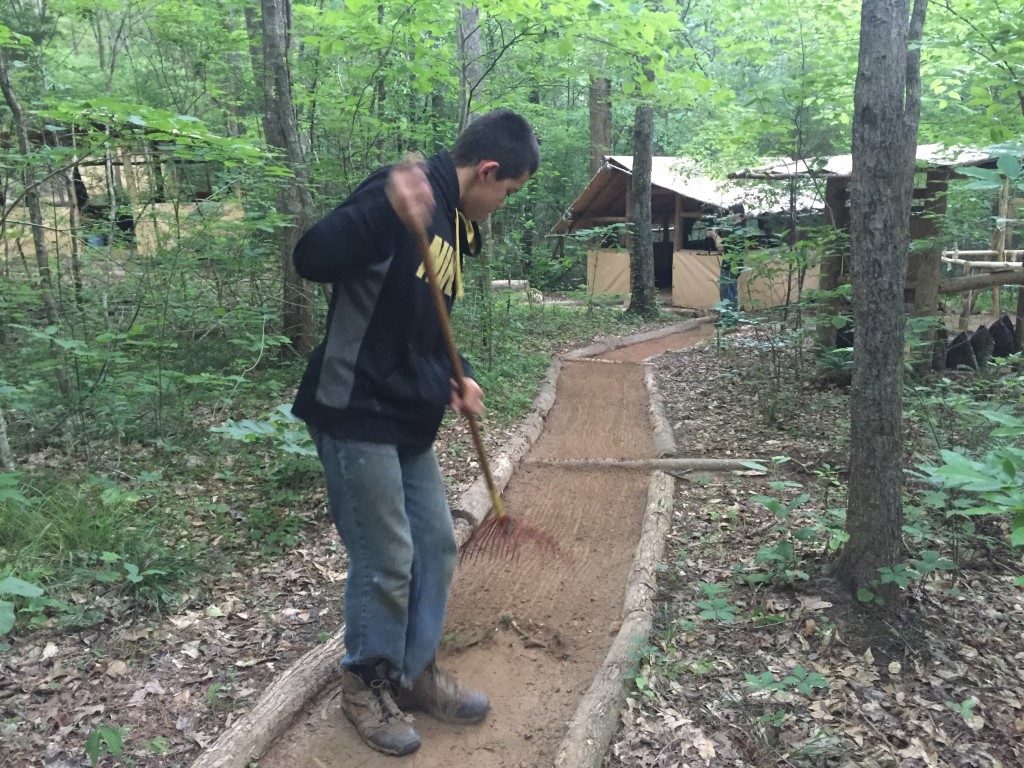 young man sweeping a trail, learning personal responsibility